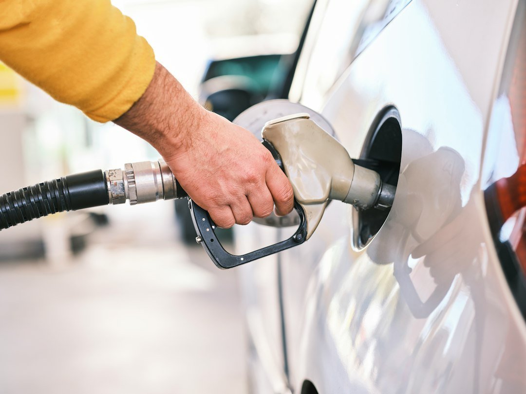 Gros plan d’une main qui fait le plein de carburant à la pompe d’une station-service. Photo d’engin akyurt, Unsplash.