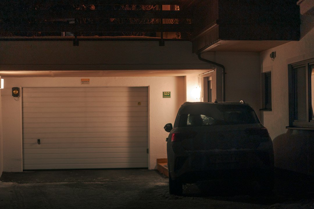 Voiture sombre garée devant un garage de maison, la nuit. Photo de BehindTheTmuna, Unsplash.