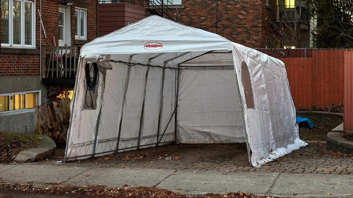 Abri de voiture démontable en toile blanche sur armature métallique, installé devant une maison en briques à la tombée du jour, en automne