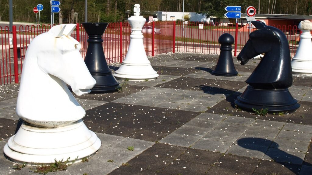 Pièces d’échecs géantes, cavaliers blanc et noir, sur un échiquier de dalles au bord d’une aire de repos de l’autoroute A6 sous un ciel dégagé