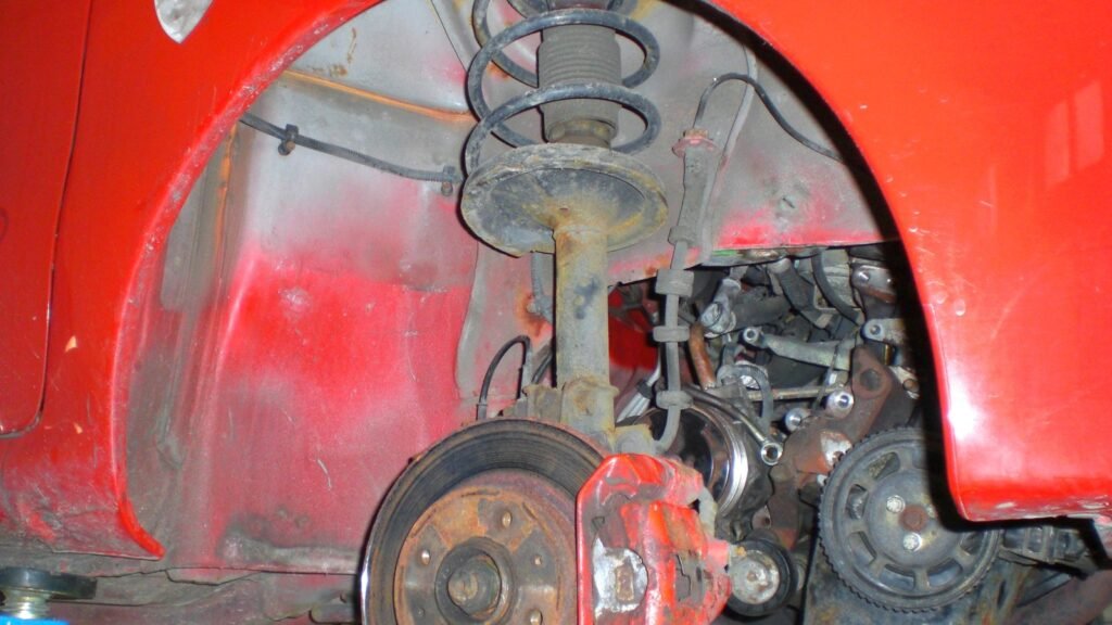 Suspension avant d’une Fiat Seicento rouge sur pont : jambe de force avec amortisseur, ressort hélicoïdal et disque de frein