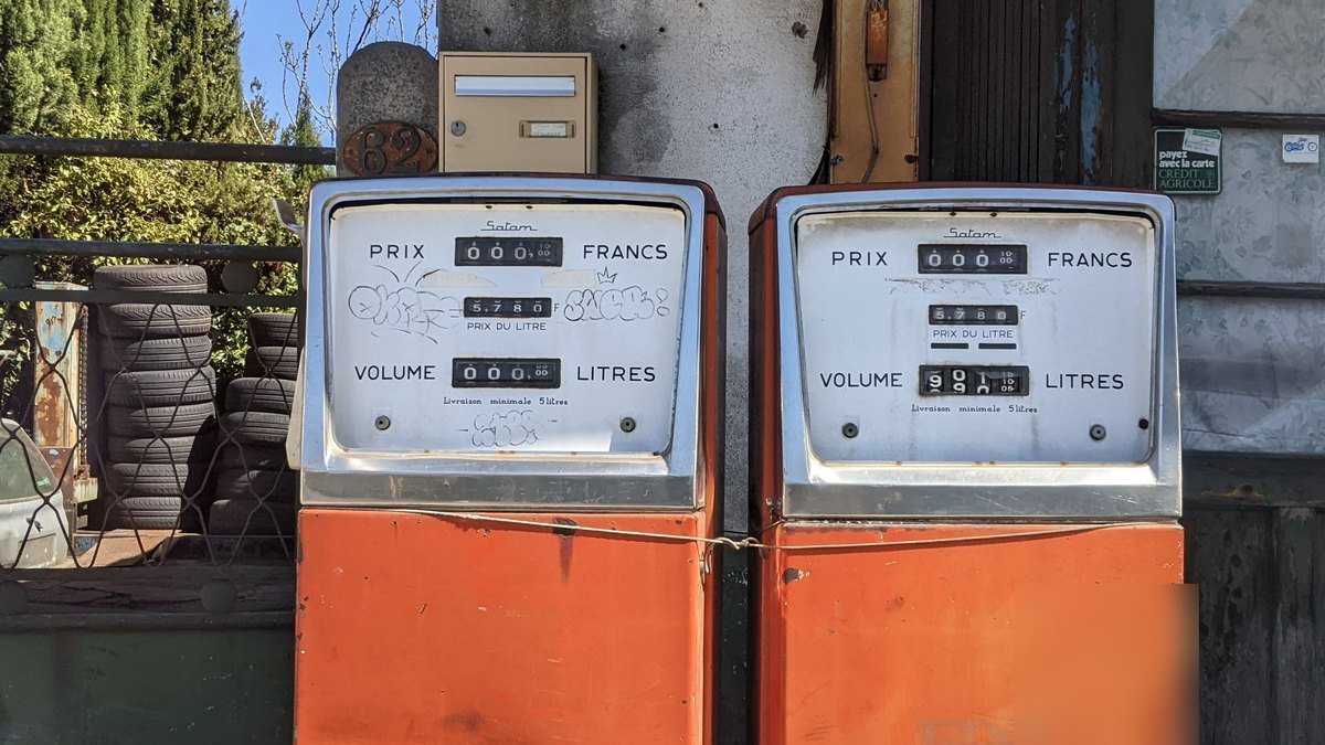 Deux anciennes pompes à essence orange devant un garage de Toulouse, avec des compteurs Prix en francs, Prix du litre et Volume en litres
