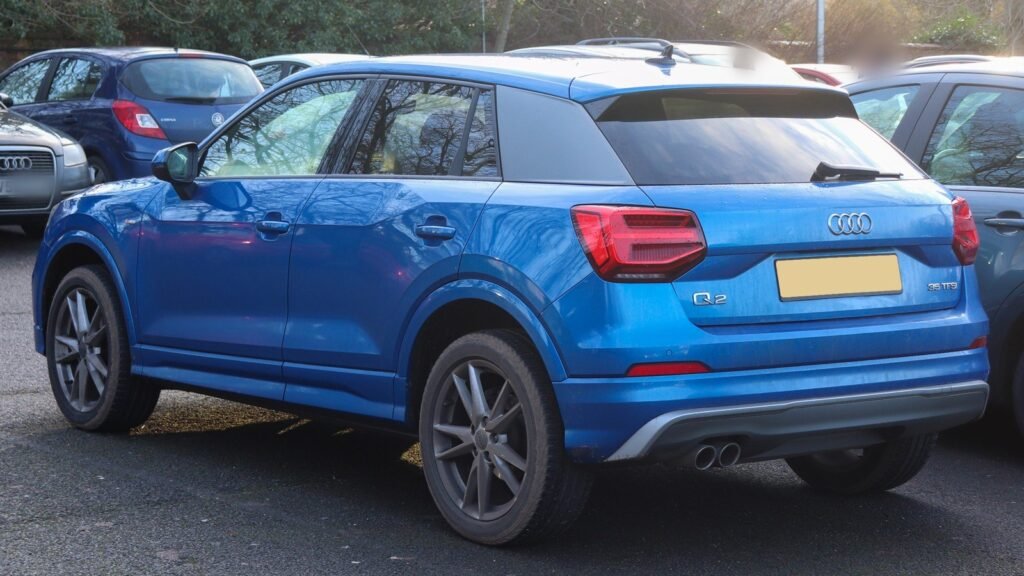 Audi Q2 bleu de 2019 vu de trois quarts arrière sur un parking, avec la lame grise contrastée du montant arrière, la pièce visée par le rappel 53D2