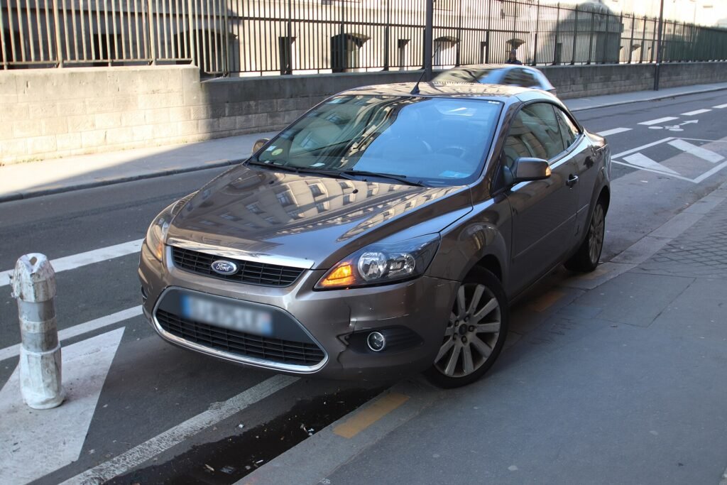 Voiture grise à pare-chocs avant enfoncé garée de travers sur une voie à Paris, symbole des petits sinistres que l’assurance auto doit couvrir