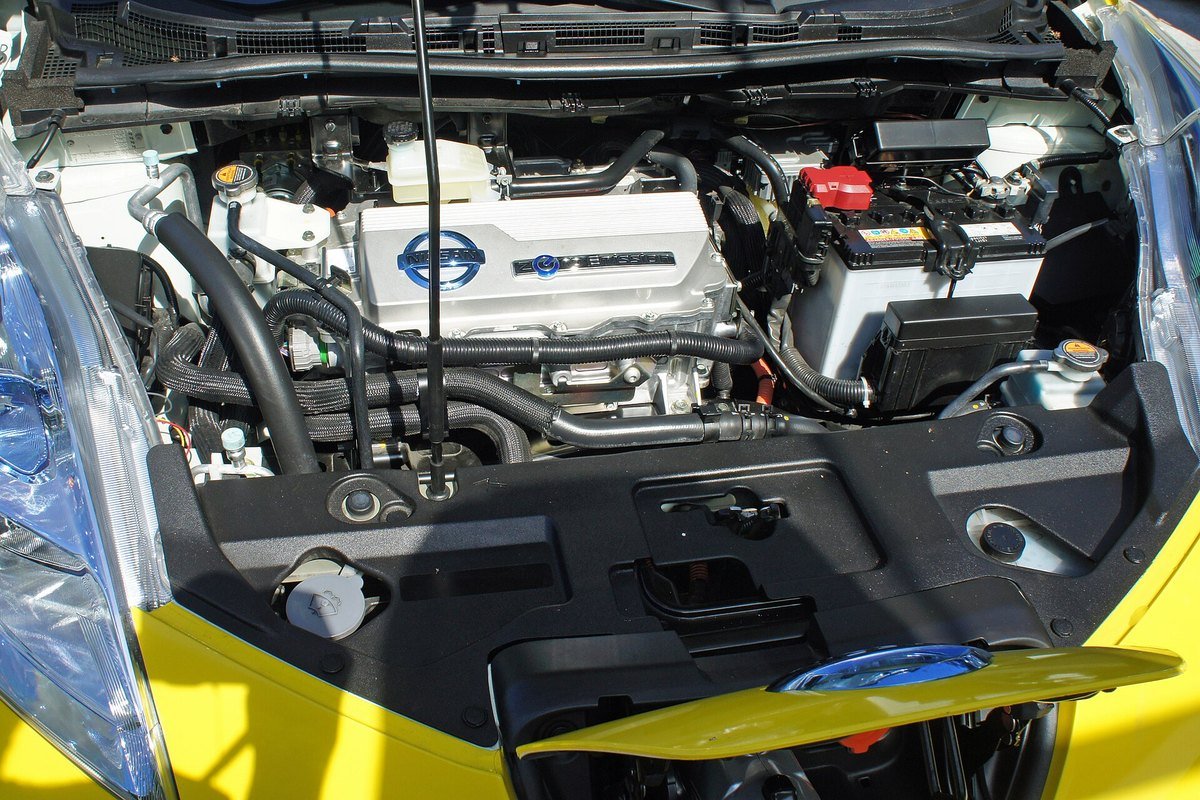 Compartiment avant d’une Nissan Leaf, capot ouvert : boîtiers électroniques au centre et batterie 12 volts au plomb sur la droite
