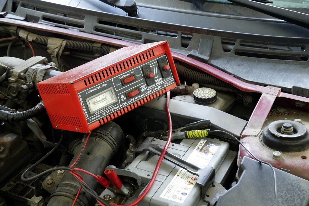 Chargeur de batterie rouge relié par ses pinces à la batterie d’une voiture, sous le capot ouvert