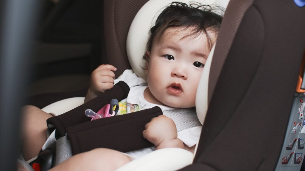 Bébé aux cheveux bruns attaché par un harnais rembourré dans un siège auto, têtière enveloppante autour de la tête, à bord d’une voiture