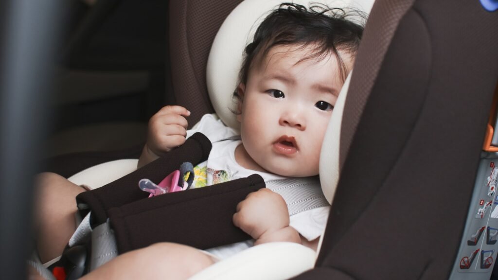 Bébé attaché dans un siège auto avec harnais et coussinets, vêtu d’un haut léger, la tétine posée sur le harnais