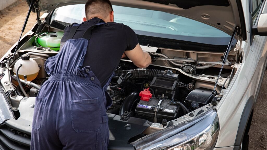 Mécanicien penché sur le compartiment moteur d'une voiture, batterie 12 V visible au premier plan