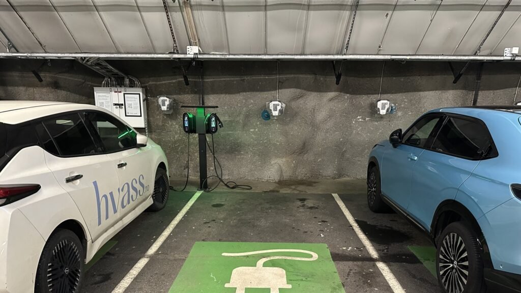 Place de parking souterrain marquée d’une prise verte, avec une borne de recharge murale au fond et deux voitures électriques de part et d’autre
