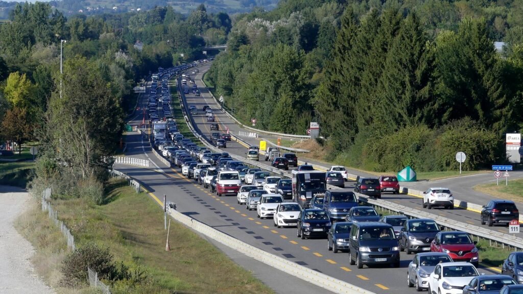 Longue file de voitures à l’arrêt sur l’autoroute A41 à Entrelacs, en Savoie, entre des collines boisées, par une fin de journée ensoleillée