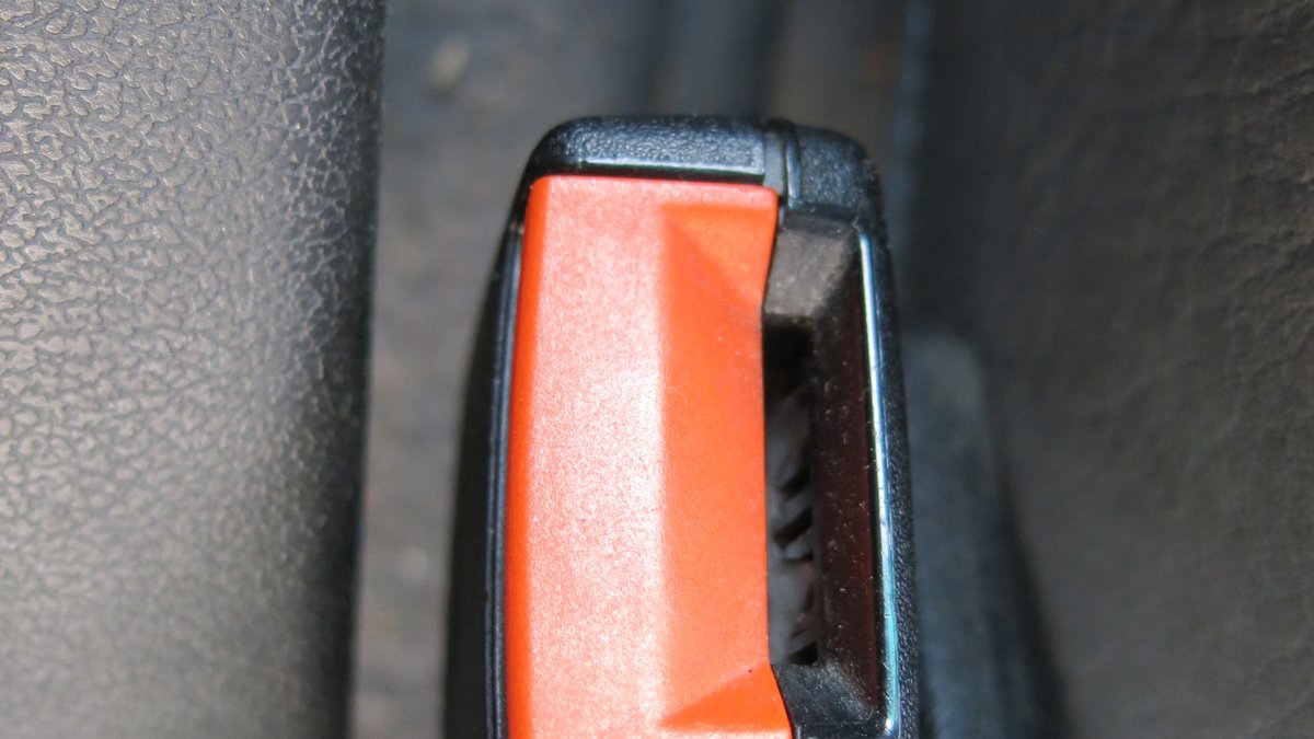 Gros plan sur la boucle d’une ceinture de sécurité de voiture avec son bouton d’ouverture rouge, sur une banquette en cuir noir