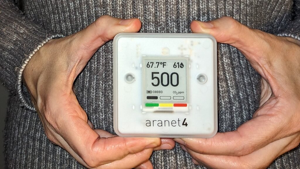 Capteur de CO2 Aranet4 tenu à deux mains, écran à encre électronique affichant 500 ppm avec une jauge verte, jaune et rouge