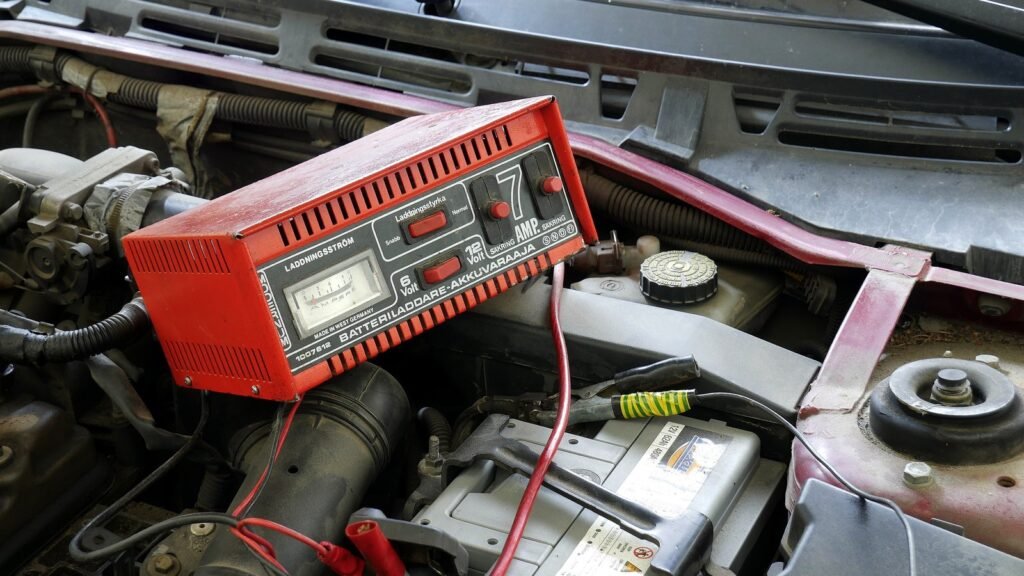 Chargeur de batterie rouge 6/12 volts de 7 ampères posé dans le compartiment moteur d’une voiture, pinces branchées sur la batterie