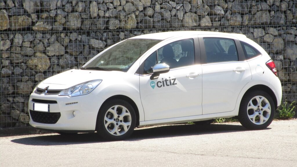 Citroën C3 de deuxième génération blanche, aux couleurs du service d’autopartage Citiz, garée devant un mur de pierres en gabions à Montmélian