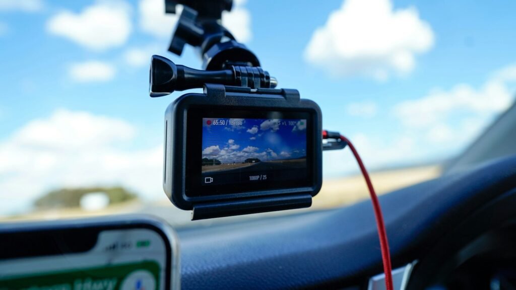 Dashcam fixée au pare-brise d’une voiture, écran allumé et câble d’alimentation rouge