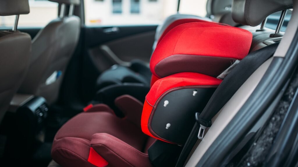 Siège auto rehausseur rouge avec dossier, fixé sur la banquette arrière d'une voiture