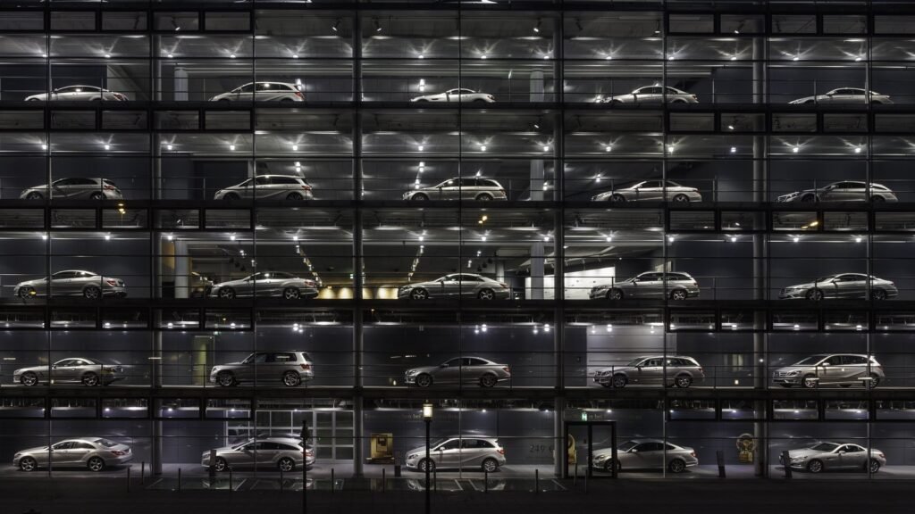 Façade vitrée d’une concession automobile éclairée de nuit, avec une trentaine de voitures grises exposées sur six étages
