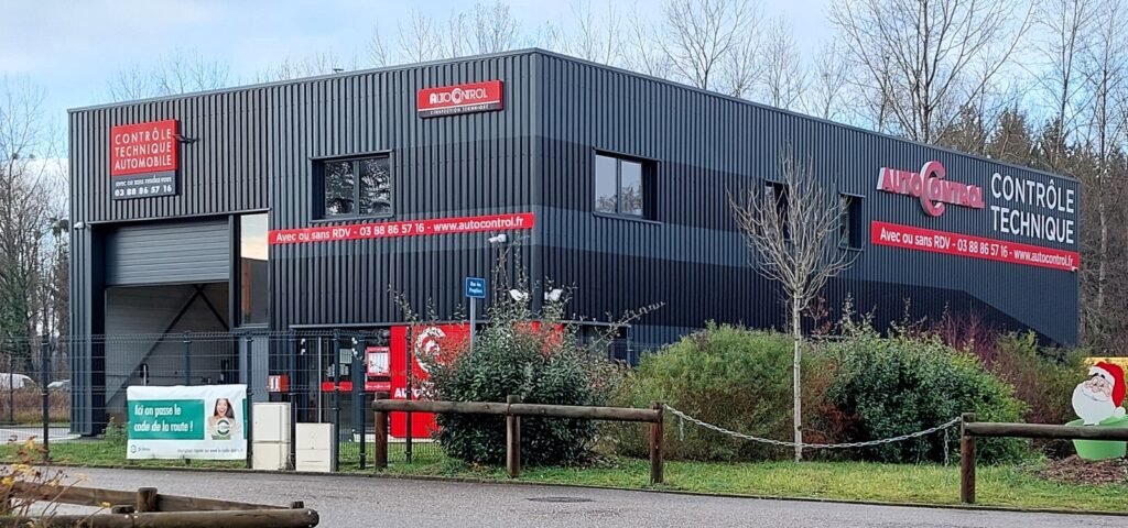 Façade d’un centre de contrôle technique automobile à Gries (Bas-Rhin), bâtiment gris anthracite avec porte de garage et enseignes rouges