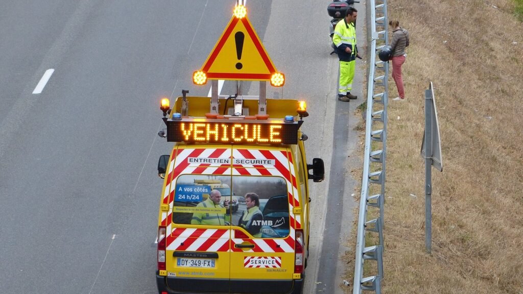 Fourgon d'intervention jaune à flèche lumineuse et panneau Véhicule, arrêté sur la bande d'arrêt d'urgence d'une autoroute, agent en gilet jaune près de la glissière
