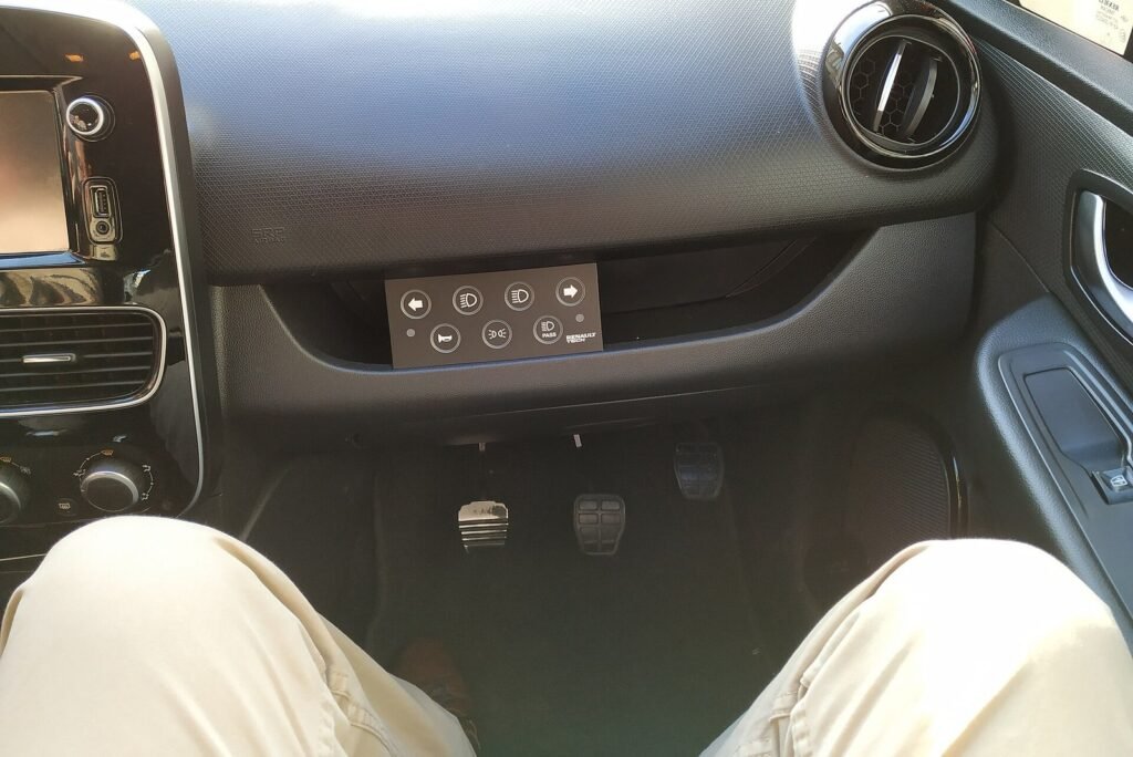 Planche de bord d’une Renault Clio d’auto-école avec boîtier de commandes du moniteur sous la boîte à gants, au-dessus des trois pédales