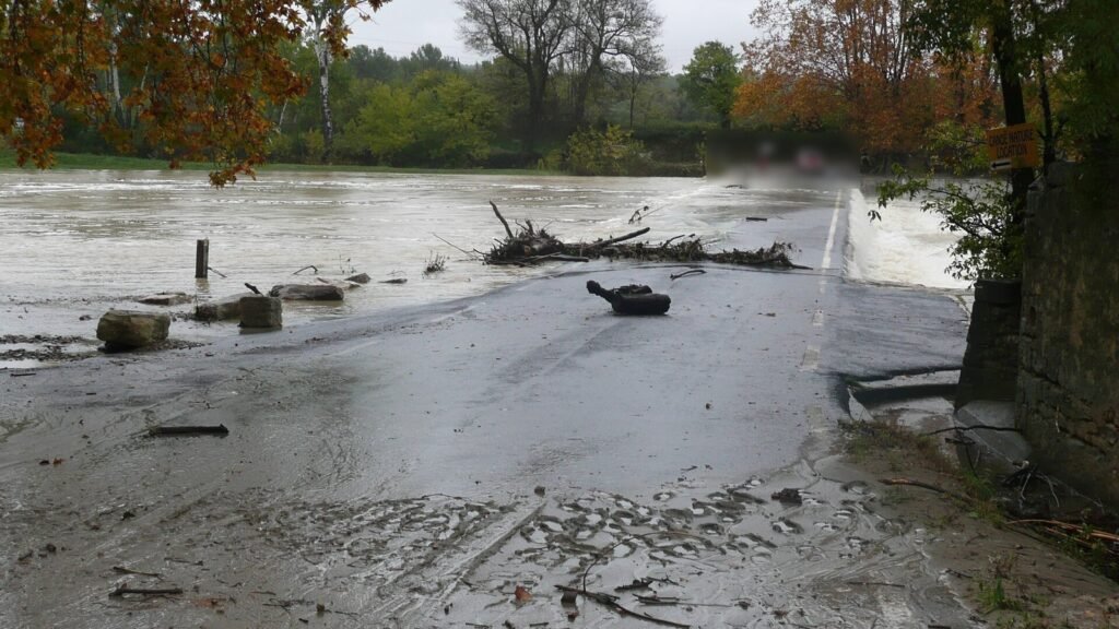 Le Vidourle en crue passe par-dessus un pont submersible à Villetelle, la route couverte de boue et de branchages, arbres aux couleurs d’automne (photo d’archive, octobre 2010)