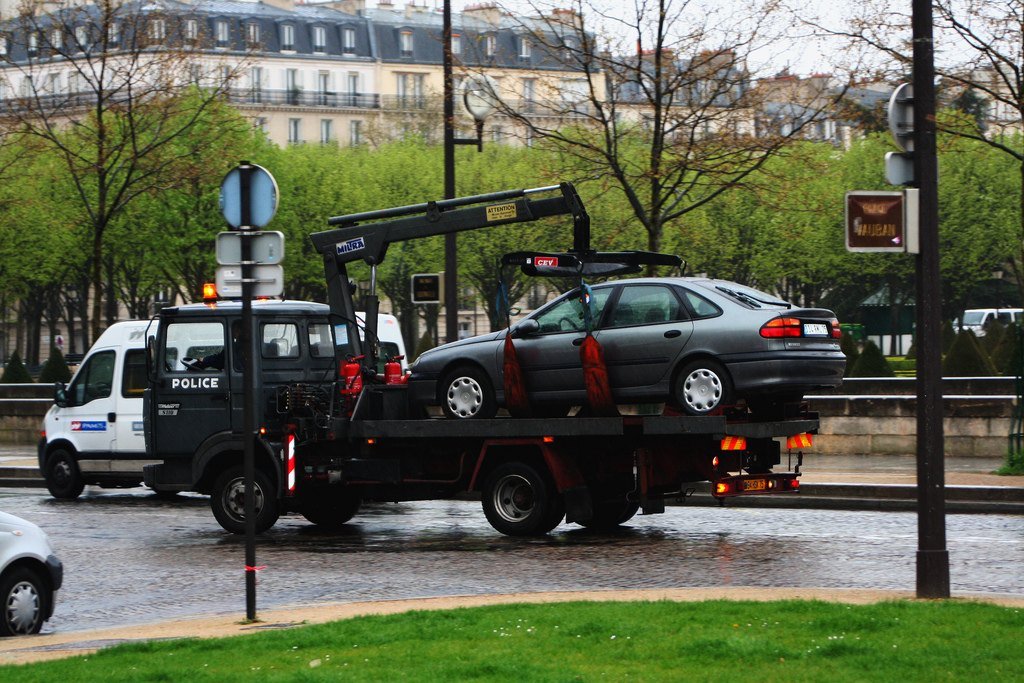 Dépanneuse de la police à Paris transportant une berline grise sur son plateau, le long d’une avenue bordée d’arbres