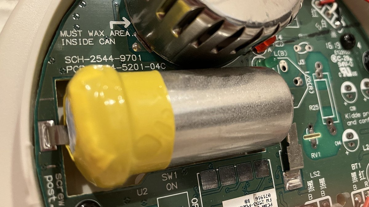 Intérieur d’un détecteur de monoxyde de carbone Kidde : cellule électrochimique cylindrique entourée d’un ruban jaune sur un circuit imprimé vert