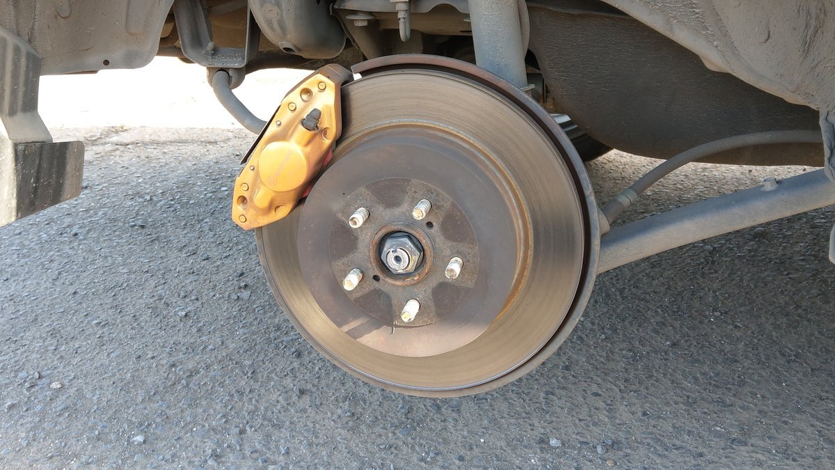 Disque de frein arrière et étrier doré d’une voiture, roue déposée, vus de côté sous le passage de roue