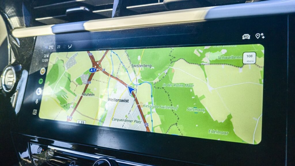 Écran tactile central d’une Opel affichant une carte de navigation OpenStreetMap avec la position du véhicule, aérateurs au-dessus et touches de commande en dessous