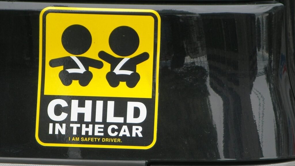Autocollant jaune et noir « Child in the car » avec deux enfants attachés, collé sur la lunette arrière noire d’une voiture