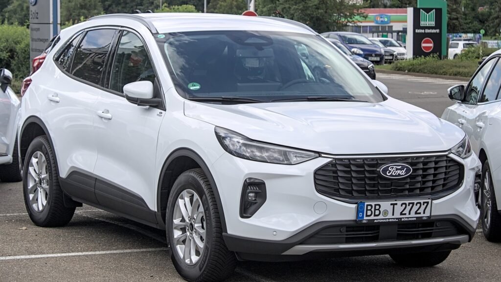 Ford Kuga blanc de troisième génération restylé, vu de trois quarts avant, garé sur un parking de concession en Allemagne