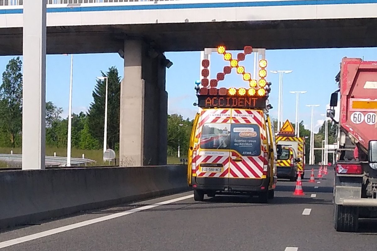 Fourgon d'intervention jaune avec flèche lumineuse et panneau Accident fermant une voie d'autoroute, cônes orange au sol