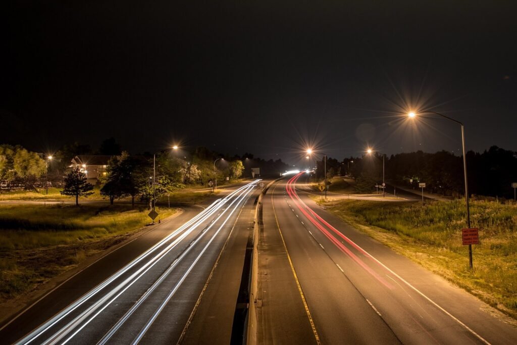 Route de nuit éclairée par des lampadaires, avec des traînées lumineuses blanches de phares et rouges de feux arrière