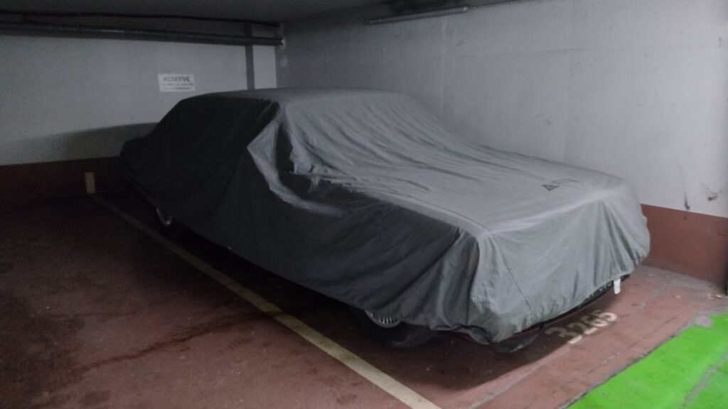 Voiture entièrement recouverte d’une housse de protection grise, garée sur une place de parking souterrain à Paris