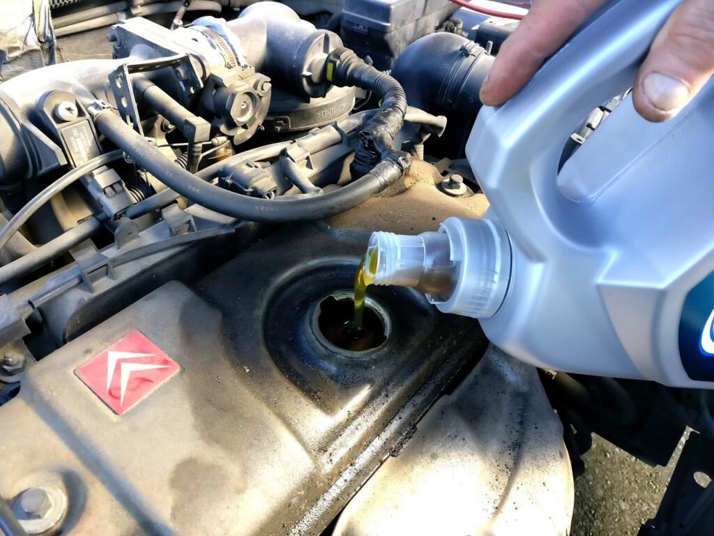 Main versant l’huile moteur dorée d’un bidon dans l’orifice de remplissage d’un moteur de Citroën, sous le capot ouvert