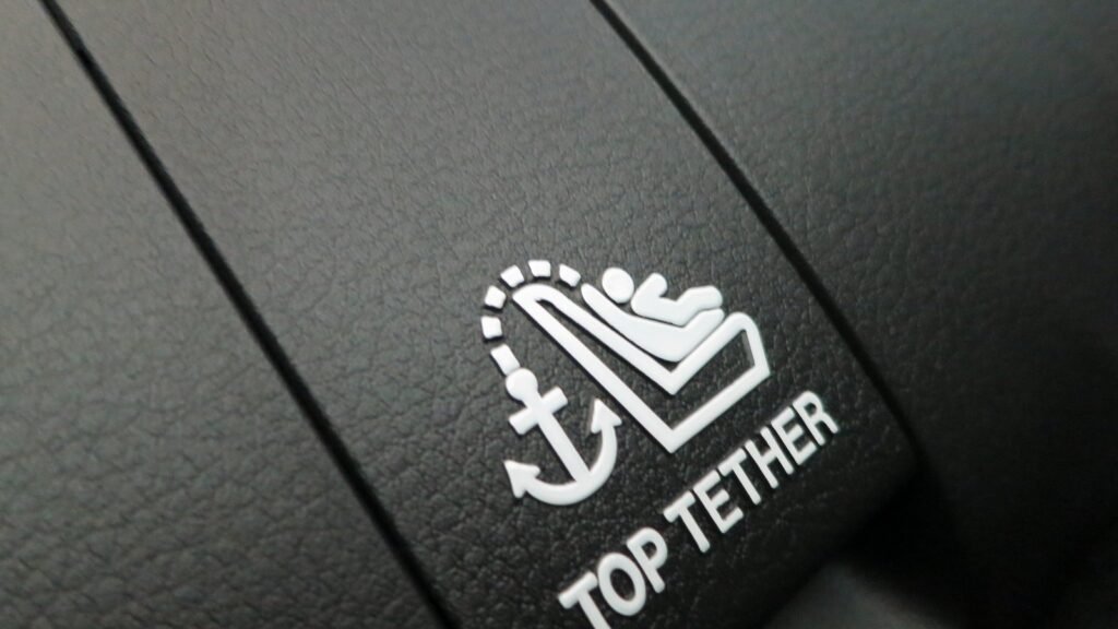 Gros plan sur un habillage noir de plage arrière de voiture portant le pictogramme blanc d’un siège enfant avec une ancre et l’inscription « TOP TETHER »