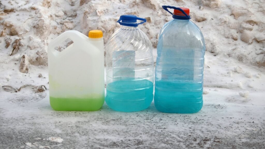Trois bidons de liquide lave-glace, un vert et deux bleus, posés sur un sol enneigé, illustration du choix d’un lave-glace d’hiver