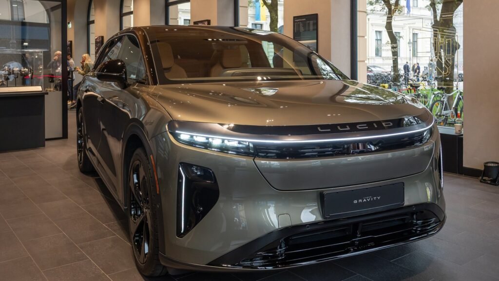 SUV électrique Lucid Gravity Grand Touring gris-vert exposé dans un showroom Lucid à Munich, vu de trois quarts avant, avec sa fine signature lumineuse
