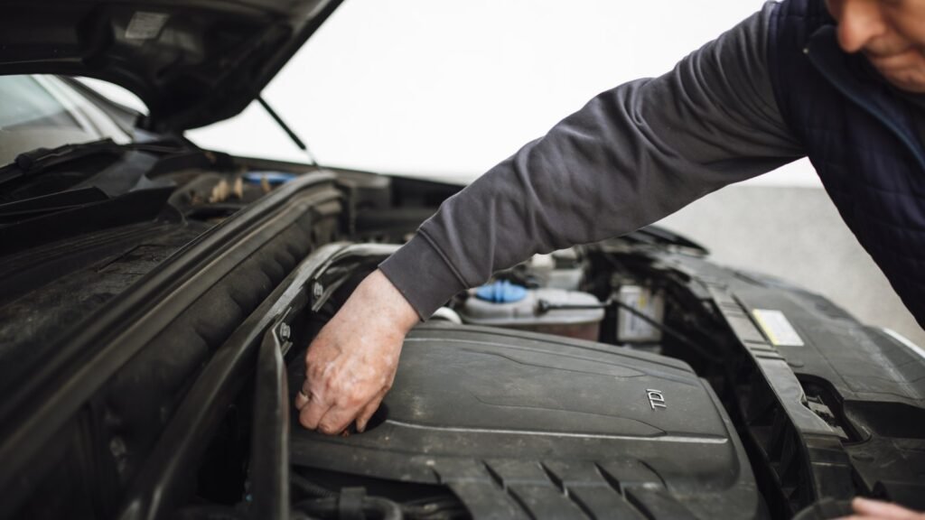 Un homme se penche sous le capot ouvert d’une voiture diesel et pose la main sur le cache du moteur pour un contrôle d’entretien