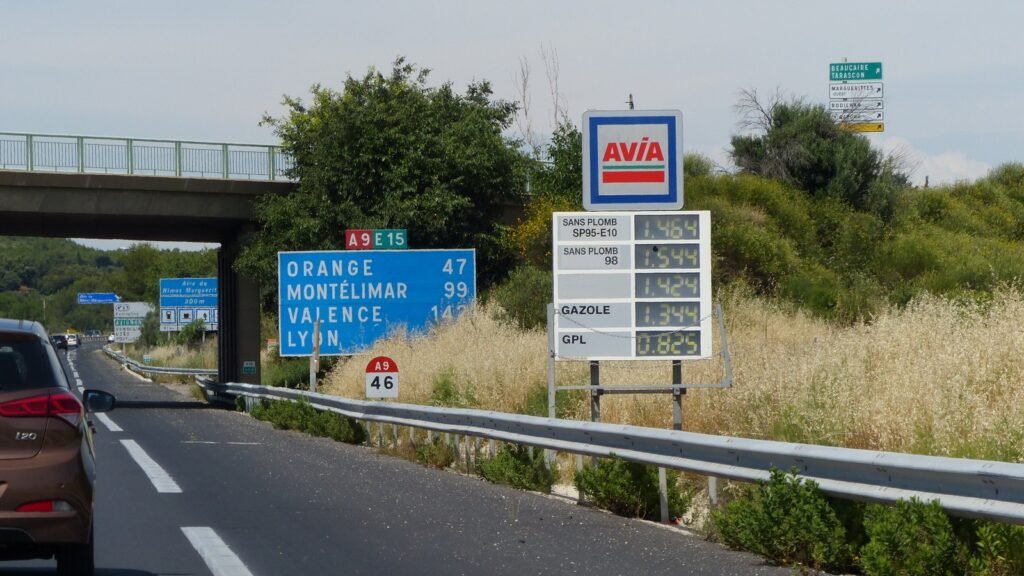 Panneau d’affichage des prix du carburant d’une station Avia au bord de l’autoroute A9, avec panneaux de direction Orange, Montélimar, Valence et Lyon