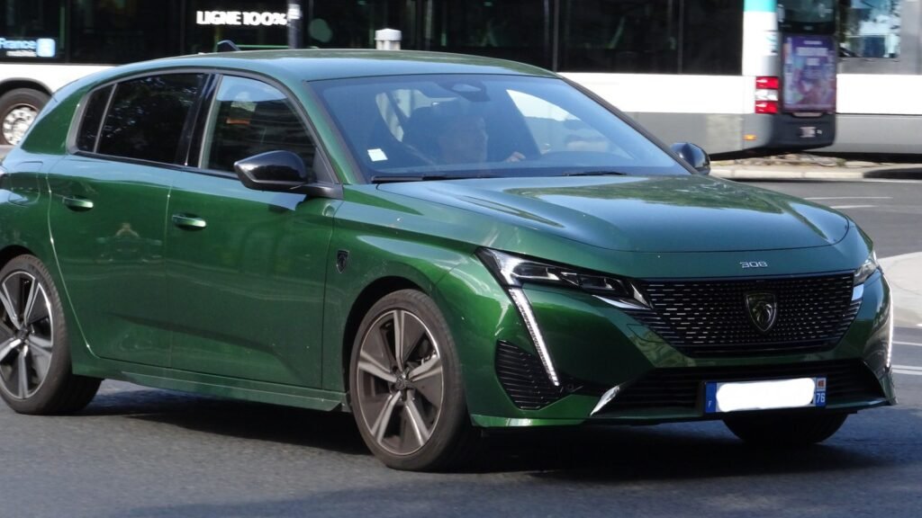 Peugeot 308 verte vue de trois quarts avant, en circulation dans une rue de Paris, avec un autobus en arrière-plan