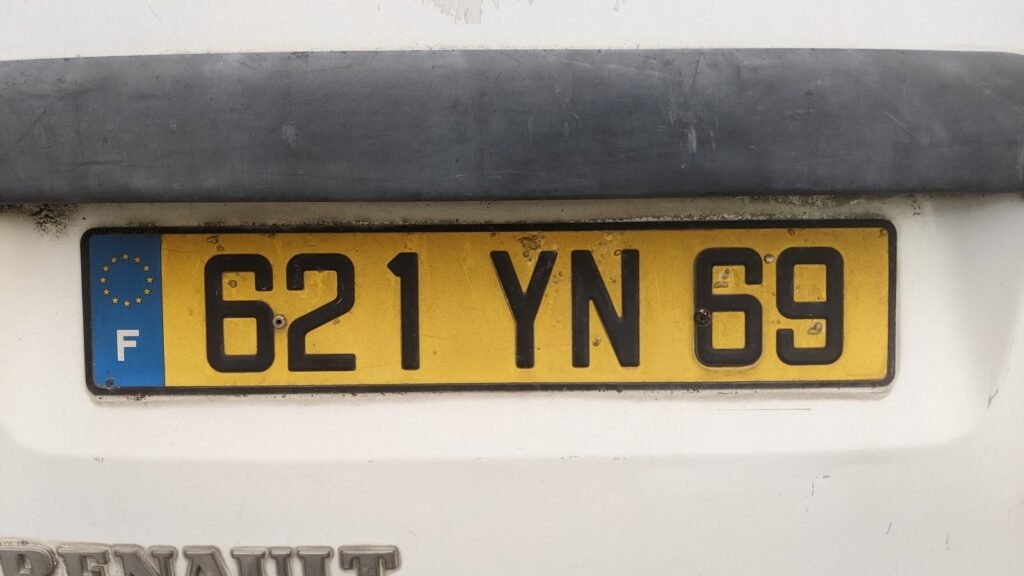 Plaque d’immatriculation jaune à l’ancien format, numéro 621 YN 69 du Rhône, à l’arrière d’un véhicule Renault blanc