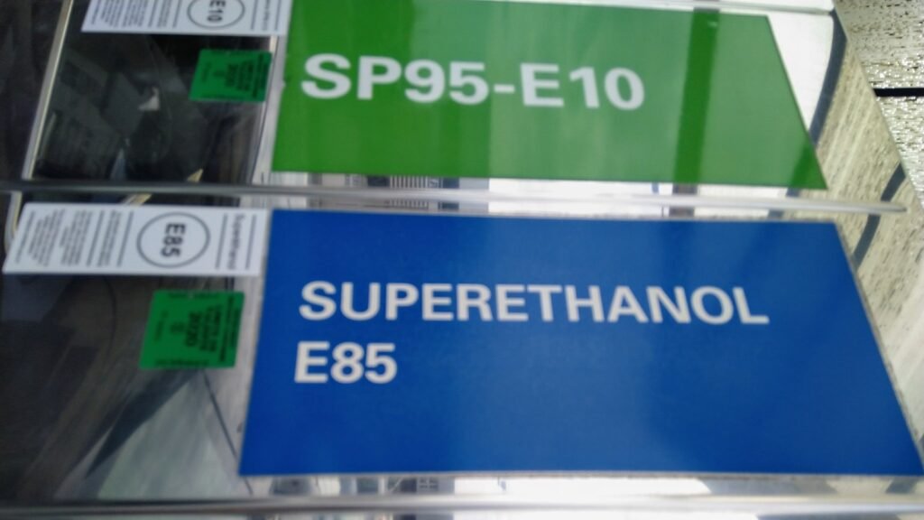 Trois panneaux de pompe dans une station française : SP95-E10 sur fond vert, Superéthanol E85 sur fond bleu et Gazole sur fond jaune