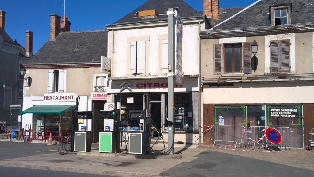 Deux pompes à gazole devant un garage Citroën dans la rue d’un village, avec un restaurant à gauche et des maisons anciennes à Vatan, dans l’Indre
