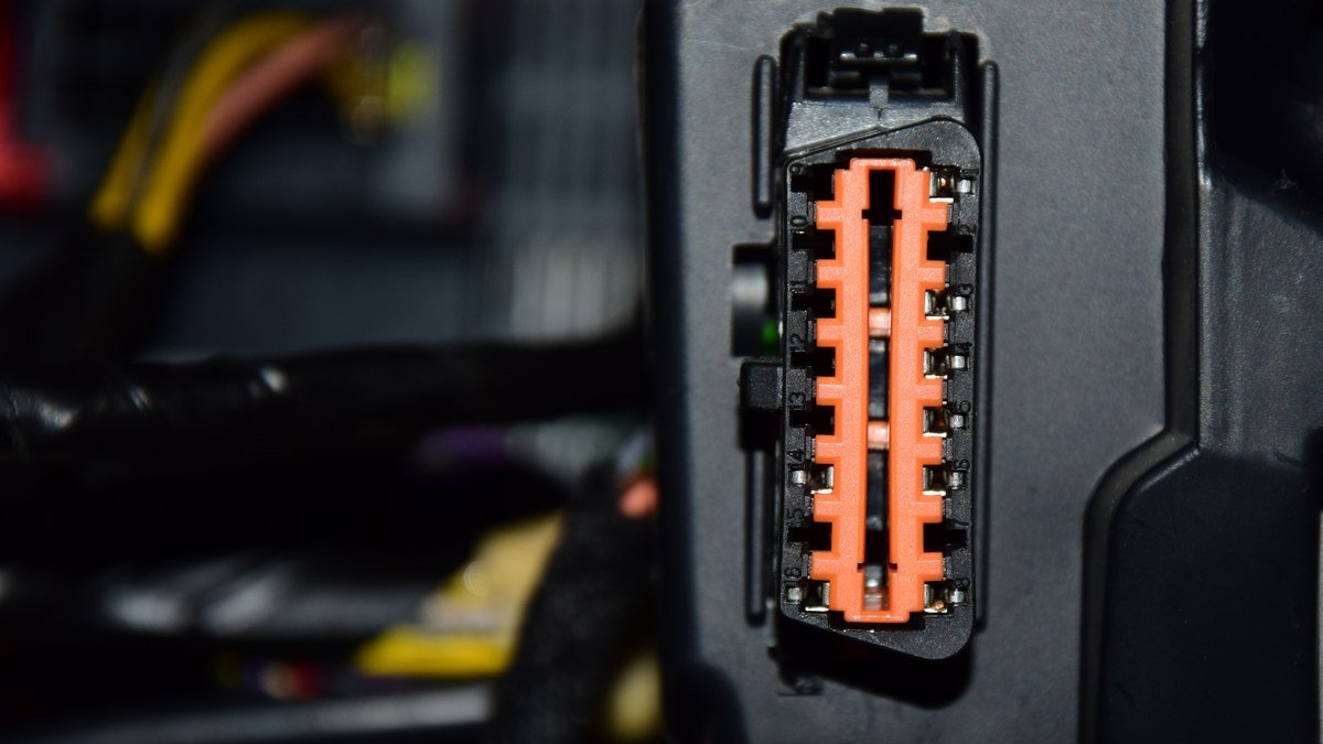 Prise de diagnostic OBD-II d’une voiture, connecteur femelle orange à 16 broches encastré sous le tableau de bord, faisceaux électriques flous à l’arrière-plan