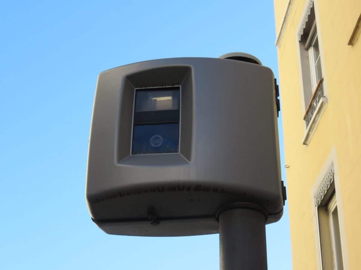 Ancien radar feu rouge gris fixé sur un poteau au bord d’une avenue de Lyon, sous un ciel bleu