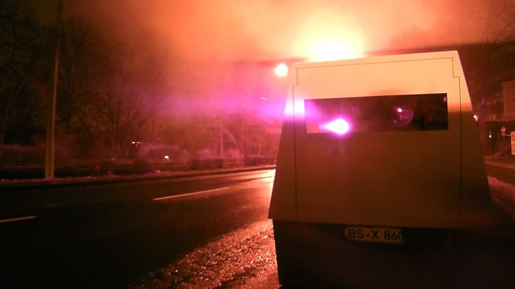 Remorque radar mobile au bord d’une avenue de nuit en Allemagne, au moment du flash rose et orange, illustration d’un contrôle de vitesse