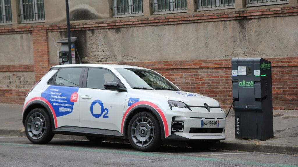 Une Renault 5 électrique blanche branchée à une borne de recharge en bordure de rue, devant un mur de briques, à Toulouse