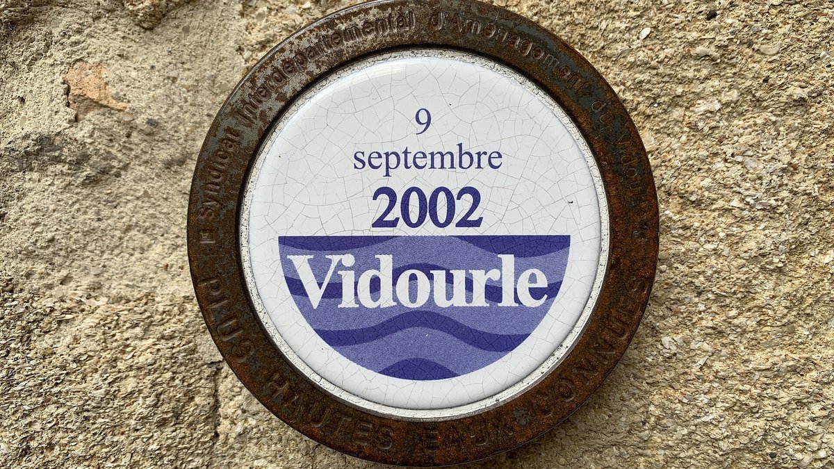 Plaque ronde en céramique scellée dans un mur à Sommières, marquant la hauteur de la crue du Vidourle du 9 septembre 2002
